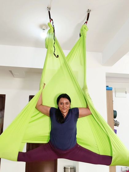 A student gracefully holds a wide-legged split in a vibrant green hammock, showcasing the flexibility gained from aerial practice.