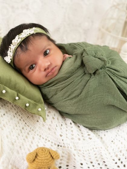 An alert 18-day-old baby girl lies on a miniature bed, looking at the camera. This pose shows that beautiful portraits are possible even when the baby is awake.