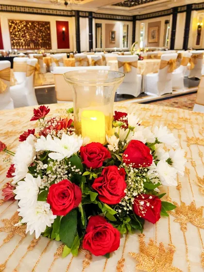 A classic and elegant low centerpiece featuring a bed of red roses and white chrysanthemums surrounding a hurricane glass with a pillar candle. This timeless design adds a romantic glow to any table.