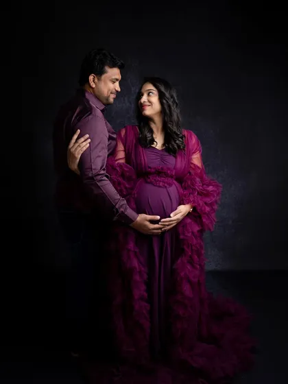 An intimate couple's pose during a maternity shoot. The dark, moody lighting and the rich color of the gown create a romantic and sophisticated portrait for the expecting parents.