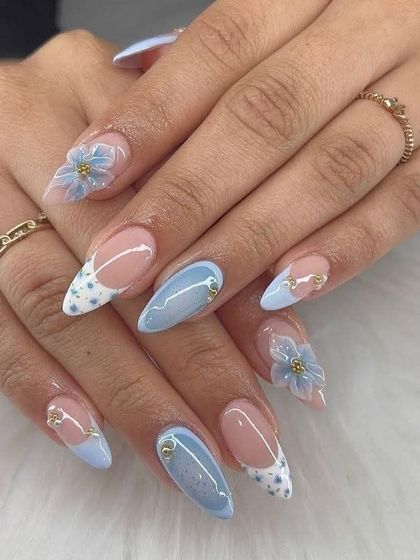 A dreamy, sky-blue nail set perfect for a vacation. It features a mix of solid blue nails, a dotted French tip, and delicate 3D blue flowers with gold bead centers for a touch of elegance.
