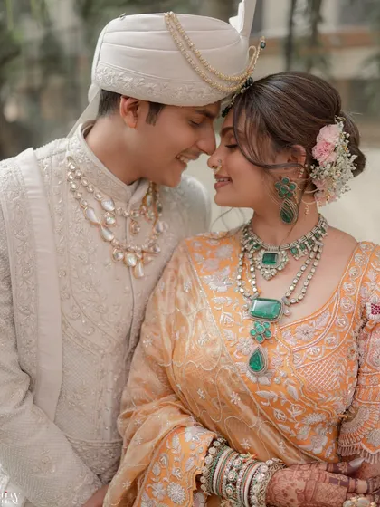 A tender close-up of the couple, highlighting the bride's stunning emerald jewelry and the groom's classic sherwani.