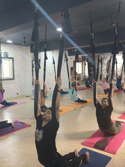 A group of students using the hammocks for a supported backbend, opening the chest and shoulders together.