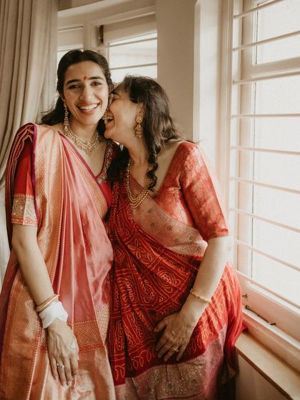 A beautiful moment between sisters, styled in coordinating shades of red and pink for a 'Mandap Muharat' ceremony. This showcases our approach to using color to create a cohesive family look.