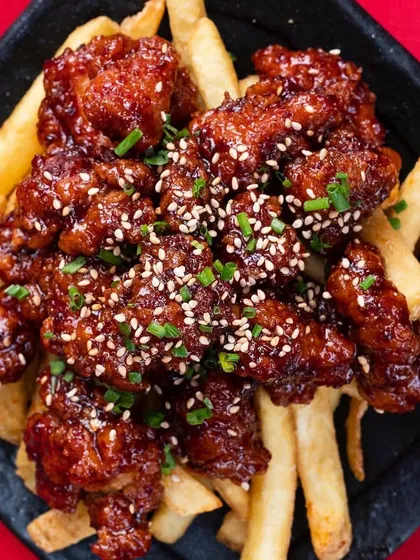 A plate of Korean Fried Chicken on a bed of fries. The top-down angle shows off the glossy sauce and sesame seed garnish.