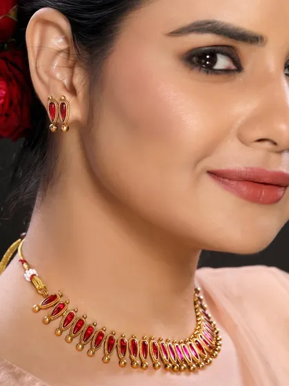 A close-up view of a model wearing a traditional gold necklace with red enamel work. The angle highlights the texture and color, providing customers with a clear look at the product.