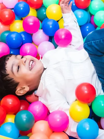 A candid shot capturing the pure joy of a young boy laughing as he plays in a colorful ball pit during his birthday party.