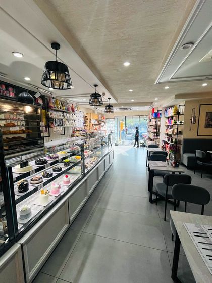 A wide view of our bakery interior, showing the long display counter filled with cakes, pastries, and savory items, with our cozy seating area in the background.