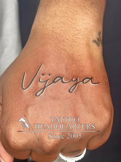 The name "Vijaya" inked in a stylish, flowing script across the back of the hand, making a bold and personal statement.