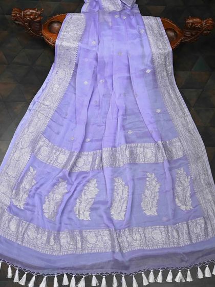 A lavender chiffon saree with a wide silver woven border. The color is soft and sophisticated, and the fabric has a beautiful, airy drape.
