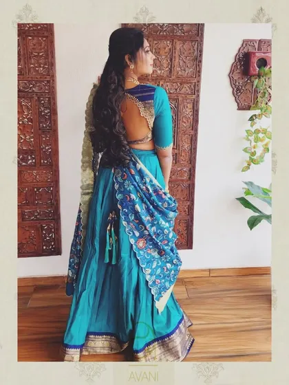 A client wearing a teal half-saree with a kalamkari print dupatta. The back of her blouse features a beautiful cutout design, adding a modern touch to the ensemble.