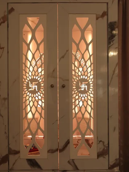 This mandir is set within a marble-finish cabinet, with intricate CNC-cut doors. The internal lighting highlights the deities and creates a warm, inviting glow.