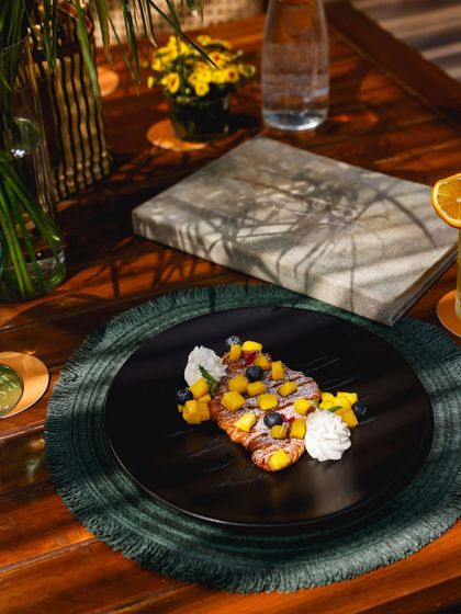 The shadows of palm leaves fall across a plate of our mango and blueberry croissant, a perfect brunch treat.