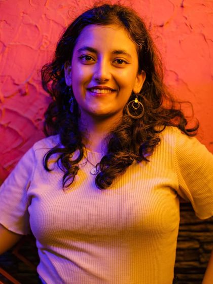 A portrait of a young woman smiling, bathed in the warm, colorful neon lights of a cafe in MKT. The red and yellow lighting creates a vibrant, atmospheric mood.