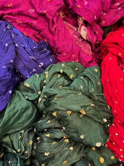 A vibrant pile of bandhani fabrics showing local shade samples of organic dyes. I explore these traditional techniques to offer a wide range of authentic colors, including deep greens, reds, and purples.