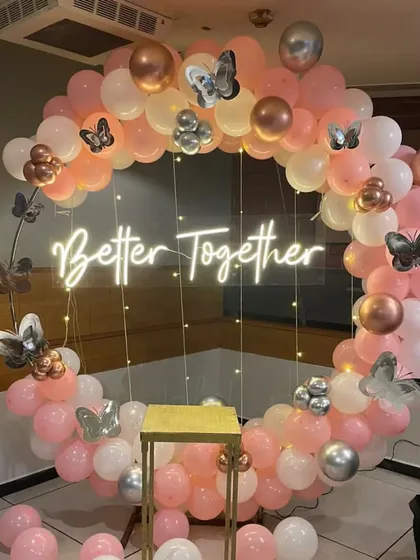A 'Better Together' celebration with a circular balloon arch in pink, white, and rose gold, accented with butterflies.