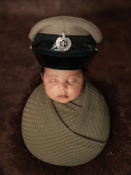 A creative and touching shot from the same session, where the newborn is safely posed wearing their father's police cap. It's a unique way to honor a family's legacy.