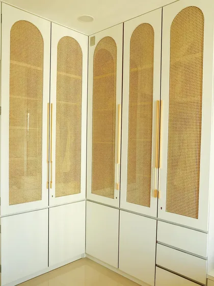 This custom L-shaped wardrobe features arched rattan panels, providing ample storage while adding a chic, airy feel to the master bedroom.