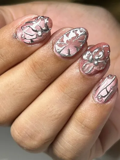 A unique 3D nail art design with a pink base and intricate silver sculpted details. The metallic elements create a futuristic, armor-like effect.