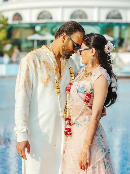 A happy, sun-kissed couple portrait after their Haldi ceremony in Vietnam, their faces covered in turmeric, sharing a loving moment by the pool.