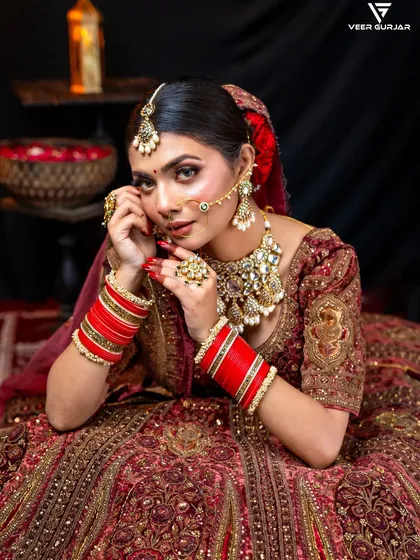 A beautiful bride showcasing her complete look. Her classic red chooda stands out against the intricate embroidery of her lehenga and complements her traditional kundan jewellery set.