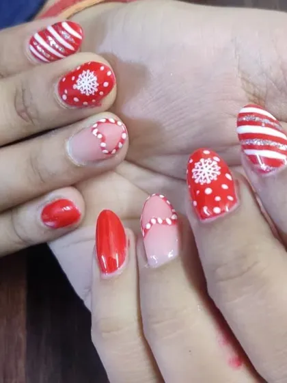 A festive Christmas-themed manicure with hand-painted snowflakes, candy cane stripes, and polka dots in red and white.