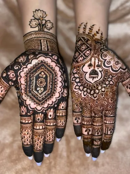 A creative fusion design. One hand has a bold, dark-filled mandala, while the other features a lighter pattern with a hanging jhumka.