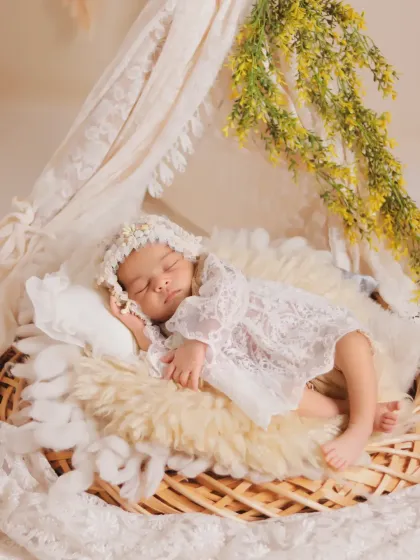 A sleeping baby in a lace outfit and bonnet, nestled in a wicker basket. This image showcases the textures and layers we use to create a cozy and visually interesting portrait.