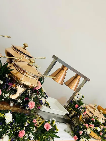 A catering table adorned with beautiful bouquets of pink, white, and purple flowers, interspersed with our signature copper chafing dishes.