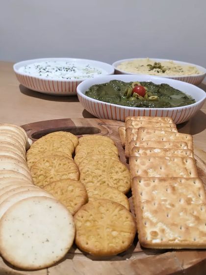 A trio of house-made dips served with an assortment of crackers. This simple yet delicious offering includes hummus, a green chutney dip, and a yogurt-based dip.