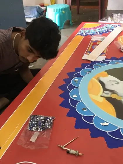 One of our artists carefully applies clay work and mirrors to a large mythological panel. This image shows the precision and steady hand required for our handmade Lippan art, ensuring every detail is perfect.