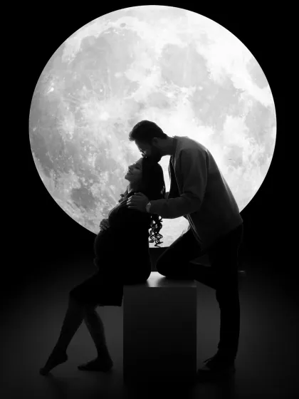 A romantic silhouette against the moon. This artistic black and white shot captures the father-to-be giving his partner a gentle kiss on the forehead.