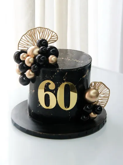 Celebrating 60 in style with this chic black and gold cake. The design features a marble effect, gold splatter, and clusters of black and gold chocolate spheres for a modern, artistic look.