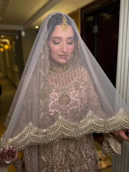A beautiful shot of the bride under her veil. The soft, diffused lighting highlights the golden hues of her outfit and the luminous quality of her skin, creating a timeless and elegant bridal portrait.