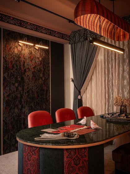 A view of the client interaction table in Zone Three. The custom table is topped with green marble and surrounded by bold red chairs, set against a backdrop of textured wallpaper panels and heavy drapes, creating a rich, layered look.