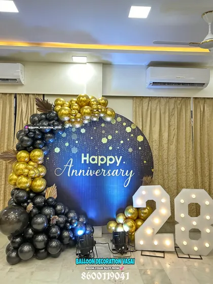 Celebrate a milestone anniversary with a statement backdrop. This design features a large circular panel with a "Happy Anniversary" message, framed by a cascade of black and gold balloons and large, illuminated marquee numbers to mark the special year.