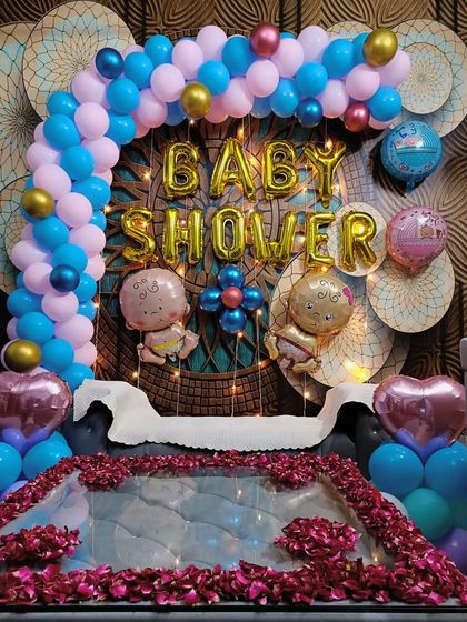 A joyful baby shower decoration. The blue and pink balloon arch, "Baby Shower" foil letters, and a floor of rose petals create a beautiful setting to celebrate the parents-to-be.