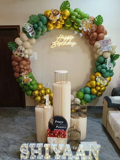 A fun and modern take on a jungle theme birthday party. This setup features a circular balloon arch in earthy greens and browns, accented with cute animal cutouts, a 'Happy Birthday' neon sign, and light-up letters for the name.