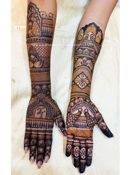 This design features the couple's initial 'H' in a beautiful script on one palm. The rest of the design is filled with royal elements like palaces, peacocks, and swans.