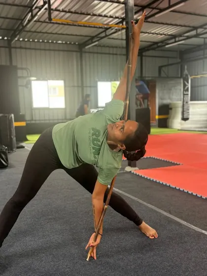 An adult student uses a stick to ensure proper alignment during a side stretch, focusing on technique.