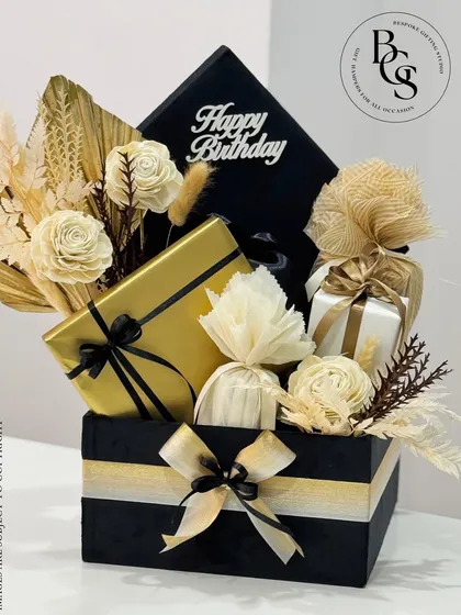 A luxurious birthday hamper designed in a sophisticated black and gold theme. The arrangement features individually wrapped gifts, complemented by dried natural botanicals like sola wood flowers and wheat stalks, creating a stunning and memorable birthday surprise.