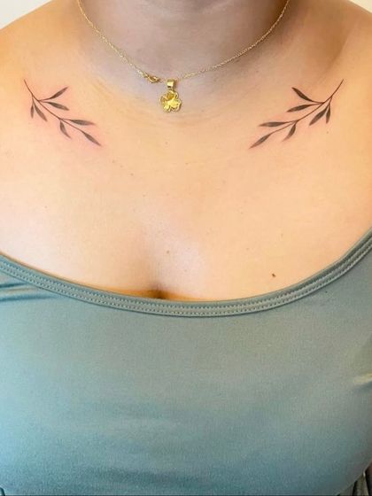 Symmetrical olive branch tattoos on each collarbone. This minimalist design creates a beautiful, balanced look.
