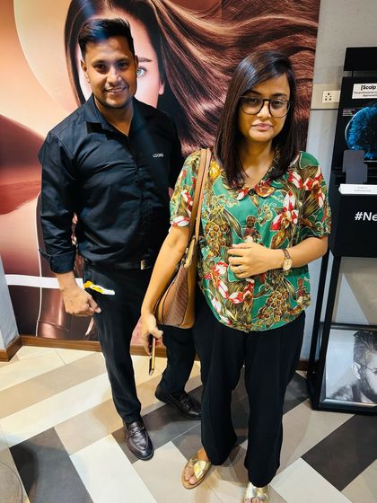 A happy client posing with her stylist after a fresh haircut and colour. Her shoulder-length hair has subtle brown highlights, giving it a healthy, refreshed look.