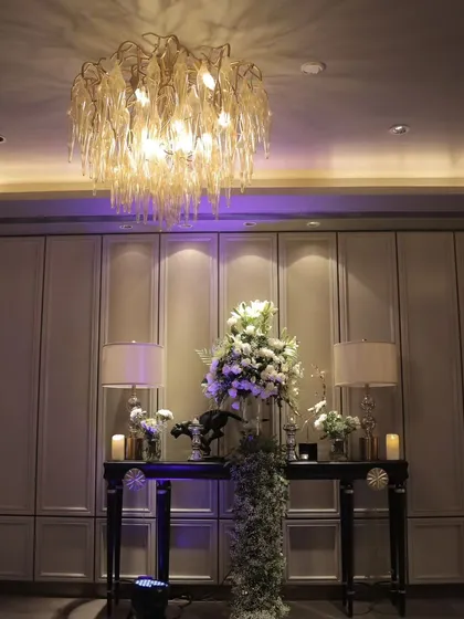 A beautifully styled console table at a reception entrance, with a large floral arrangement, elegant table lamps, and candles to create a warm and welcoming first impression.