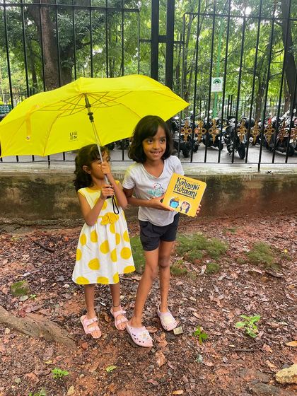 Two sisters holding a book and an umbrella on a rainy day. This sweet image captures the resilience and joy of our youngest members, determined to enjoy stories no matter the weather.