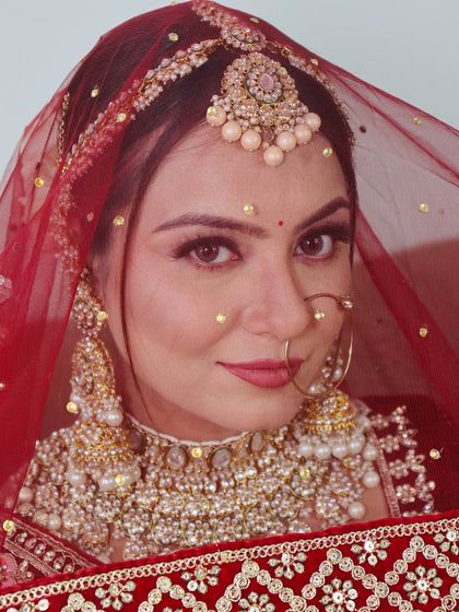 A classic bridal portrait. This look features a bold red lip and defined eyes, perfectly framed by a traditional red dupatta with pearl details.