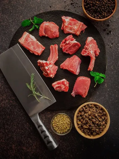 Chopped raw meat arranged on a dark surface with a cleaver and bowls of spices. The dark, contrasting background makes the red of the meat pop, creating a powerful and primal image.