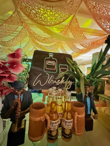A rustic 'Whiskey' station sign, paired with Corona beers in wooden mugs and jazz musician figurines for a cool, eclectic vibe.