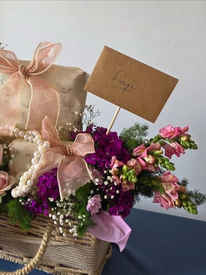 A closer look at the details, showing a handwritten note and the interplay of textures between the rustic wicker basket, soft ribbons, and delicate flowers.
