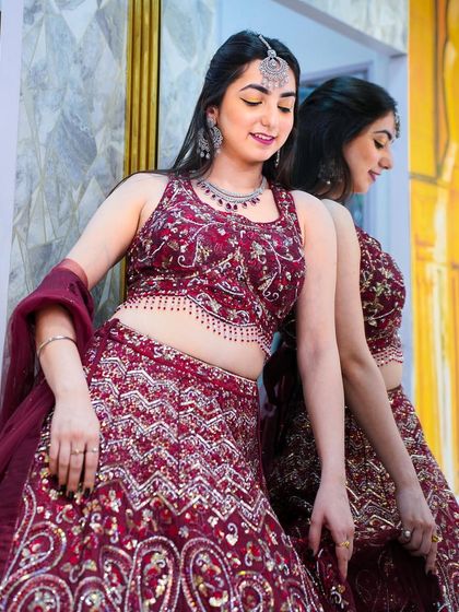 A side profile in a rich maroon lehenga, showing the detailed embroidery and the flattering fit of the blouse.